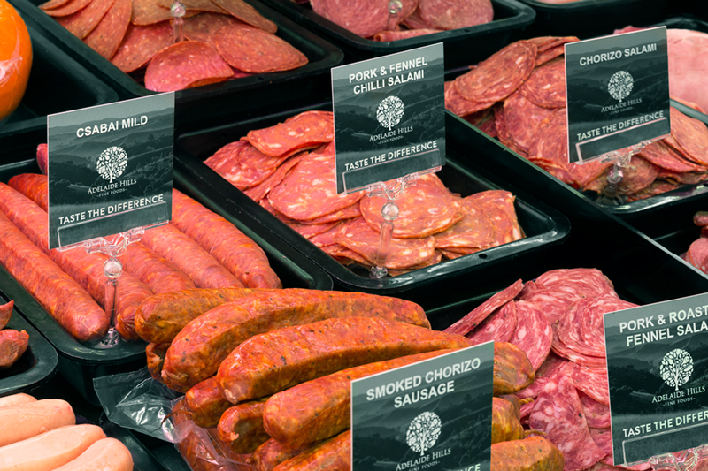 Deli cabinet showing Adelaide hills fine foods salami slices and whole chorizo sausages